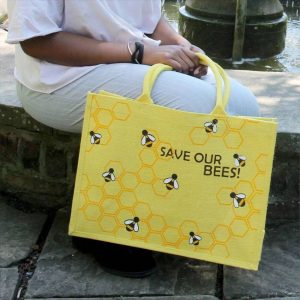 Save Our Bees jute shopping bag being carried outdoors by its yellow handles
