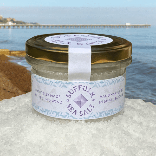 Jar of Suffolk Sea Salt displayed on sea salt crystals with Southwold Pier in the background